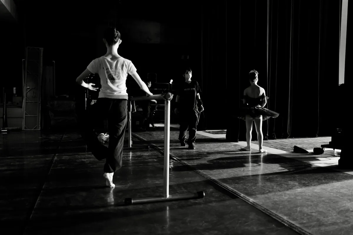 Sala de ensayo con barra fija junto a la pared y un grupo trabajando sobre suelo continuo de danza
